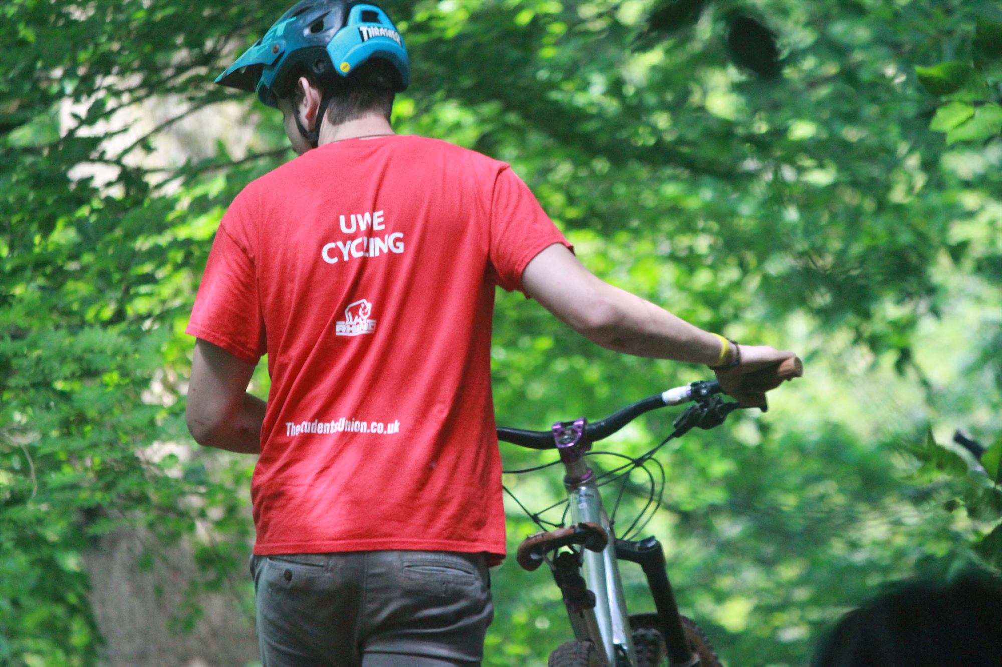 A UWE Cycling Club rider pushing a bike up a wooded trail